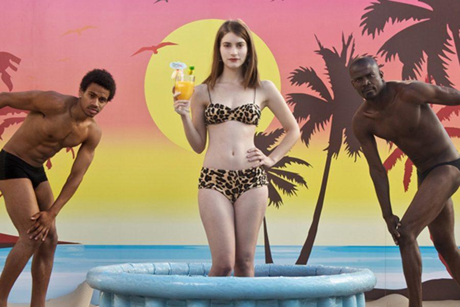 Alicia Rodríguez como Daniela Ramírez rodeada por dos modelos masculinos mientras sujeta un coctel dentro de una piscina de plástico con un fondo tropical y un bikini de animal print de la película Joven y Alocada