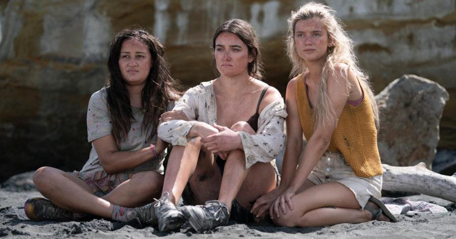 En esta imagen vemos tres protagonistas de Salvajes (The Wilds) sentadas en la arena, manchadas con tierra y despeinadas. De izquierda a derecha: Martha, Leah y Shelby. Esta serie la puedes ver en Amazon Prime